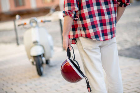 Stylish helmet. A man preparing to ride his scooter and holding a helmet
