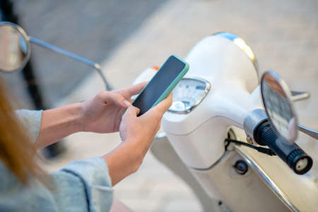 Urgent message. A woman making a stop for texting while riding a scooterの写真素材
