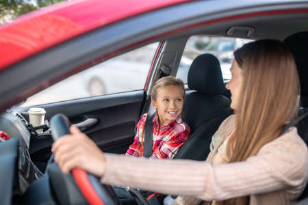 Lovely motherhood. Smiling mom sitting at the wheel, looking at her daughterの写真素材