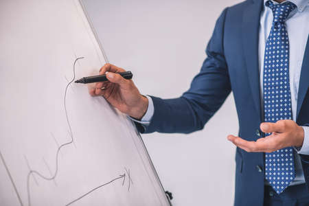 Success chart. Male hands in business jacket showing graph drawn with marker on white stand in officeの写真素材