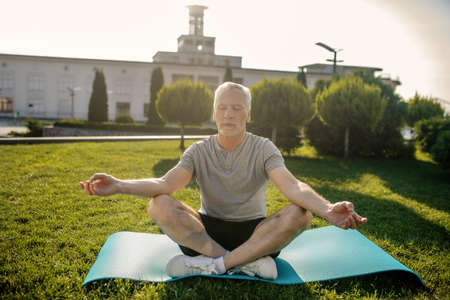 Peaceful meditation. Grey-haired man sitting in lotus pose with closed eyes and hands in Gyan mudraの写真素材