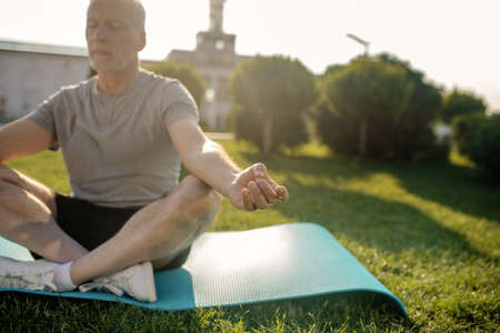 Peaceful meditation. Grey-haired man sitting in lotus pose outside, hands in Gyan mudraの写真素材