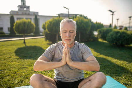 Peaceful meditation. Grey-haired man practicing yoga outside, hands in namasteの写真素材