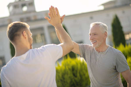 Morning workout. Young brown-haired male and grey-haired male giving high five, smilingの写真素材