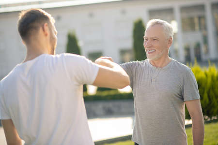 Morning workout. Young brown-haired male and mature grey-haired male touching their fistsの写真素材