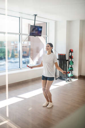 Body workout. Smiling dark-haired female jumping with skip rope in the gym