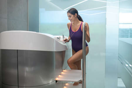 Body treatment. Dark-haired female in purple swimming suit getting into hydromassage bathtub