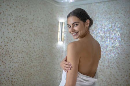 Body care. Rear view of smiling dark-haired female wrapped in towelの写真素材