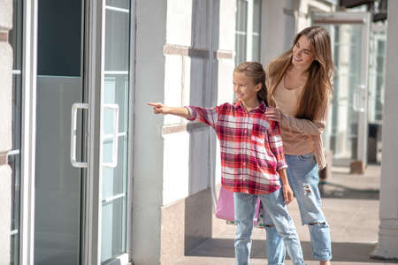 Happy moments. Smiling mom hugging her daughter pointing at the doorの写真素材