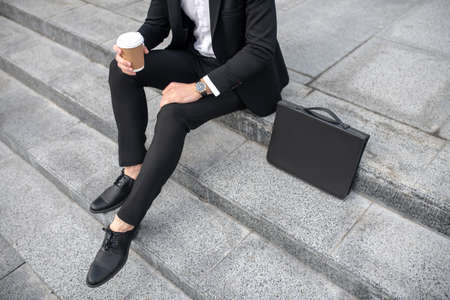 Coffee time. Close up of a man in black suit with a coffee cup in handの写真素材