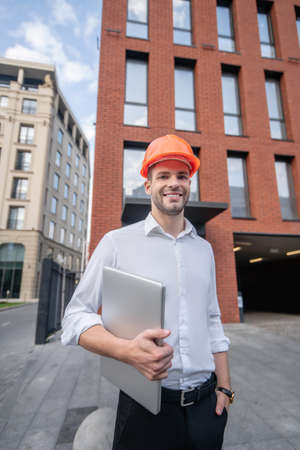 Male engineer. Male engineer in protective helmet standing near the building and smilingの写真素材