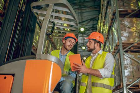 Talking. Two warehouse workers in helmets having a conversationの写真素材