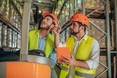 Work issues. Two warehouse workers in helmets having a work conversationの写真素材