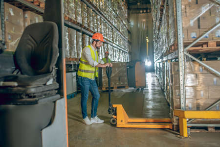 Before loading. Worker in a vest and helmet standing in the warehouse with a loaderの写真素材