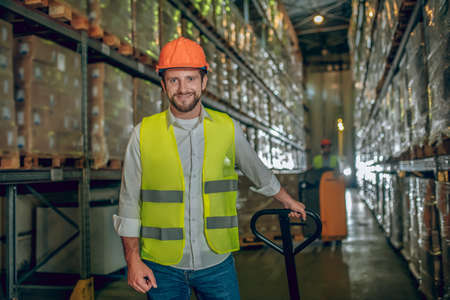 At the warehouse. Worker in a yellow vest and helmet looking positiveの写真素材