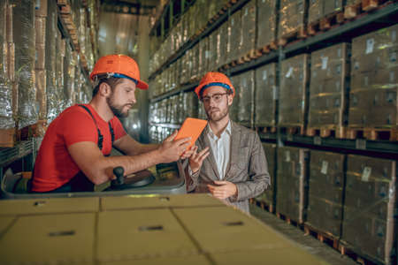 Data check. Warehouse worker showing data from internet to the warehouse managerの写真素材