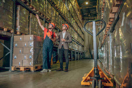 Warehouse. Warehouse worker in working clothes showing something to managerの写真素材