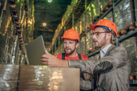 Online. Warehouse worker and manager checking the data on the laptop
