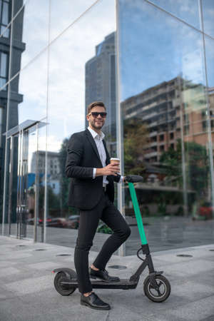 Morning coffee. Young businessman in sunglasses with the scooter having coffeeの写真素材