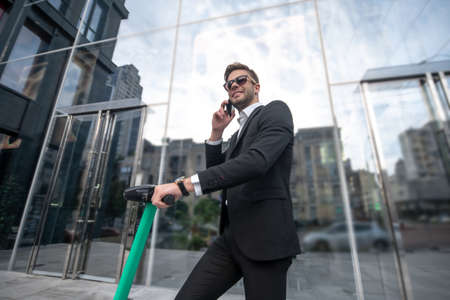 City life. Man on a scooter in sunglasses talking on the phone and looking busyの写真素材