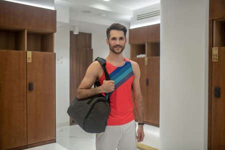 At the gym. Sporty young man in bright tshirt staning in changing room