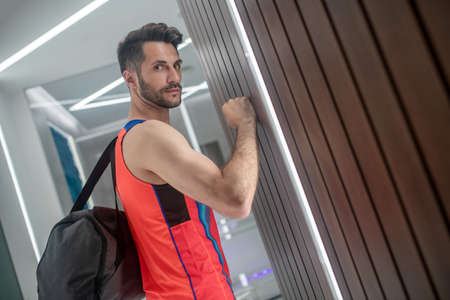 In the corridor. Sporty man in bright tshirt with a black bag in the corridor