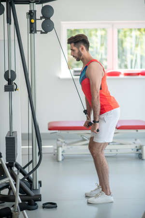 Workout. Young dark-haired man pulling the ropes and looking concentrated