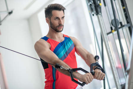 Workout. Dark-haired man working on his arms in the gym and looking concentrated
