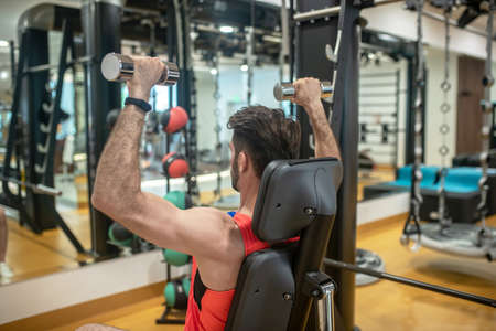 Workout in gym. Dark-haired man working on his arms on a gym machine