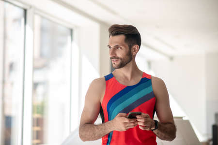 With smartphone. Sporty man in bright tshirt looking at the window