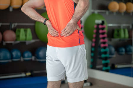 Feeling unwell. Close-up of male hands touching painful back in the gym
