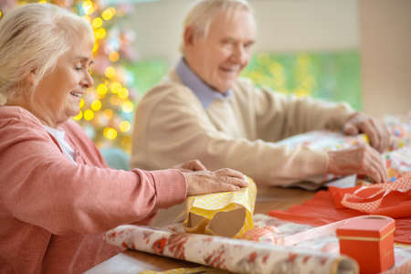 Christmas time. Elderly couple packing christmas gifts and looking contentedの写真素材