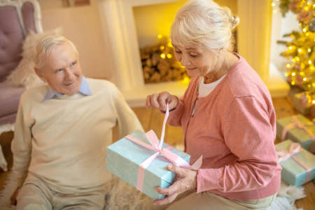 Anticipation. Elderly woman opening christmas gift from her husband and looking anticipatedの写真素材