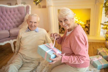 Beaming woman. Elderly woman opening christmas gift from her husband and smiling nicelyの写真素材