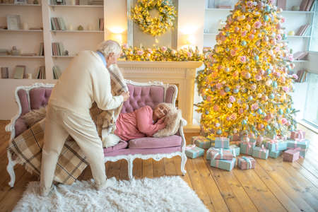 Caring husband. Grey-haired man covering his napping wife with a plaidの写真素材