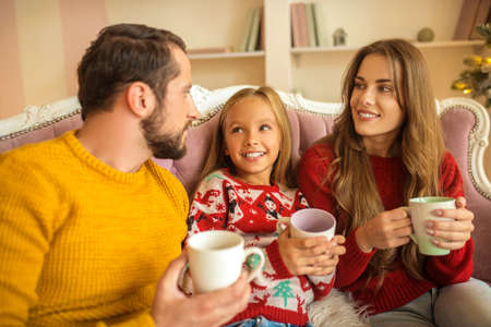 Having tea together. Young family sitting on the sofa and feeling comfortableの写真素材