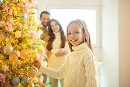 Holiday. Pretty fair-haired girl decorating new year tree with her parentsの写真素材