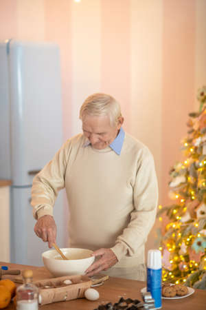 Cooking. Grey-haired man cooking in the kitchen and stirring something in a bowlの写真素材