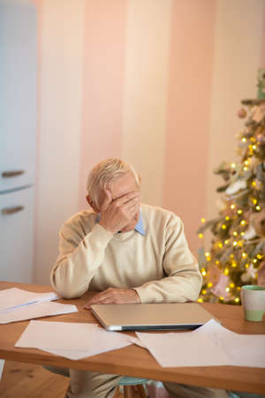 Tired. Elderly man sitting at the table and feeling tired