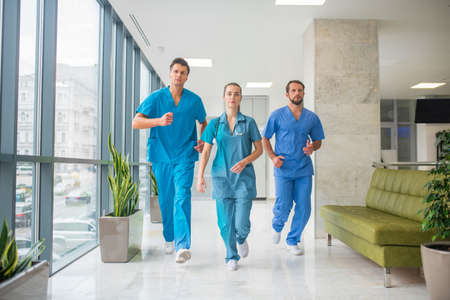 Urgent case. Three doctors running through the hospital corridor being in a hurryの写真素材