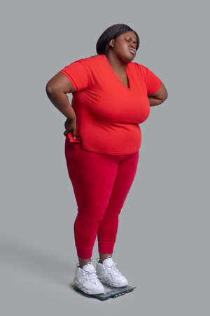 Disappointed. Young dark-skinned woman in red clothes checking weight and feeling disappointedの写真素材