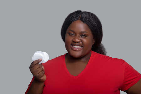 Face care. Young dark-skinned woman in red clothes holding sponge for face cleansing
