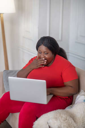 Surprised. African american woman sitting in her room with a laptop and looking surprised