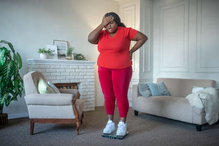 Overweight. Plus size african american woman checking her weight and looking frustrated