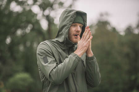 Rain. Young man in a green coat standing in the rainの写真素材