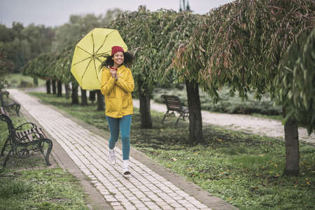 Happy moment. Cute mulatta with yellow umbrella running in the rain
