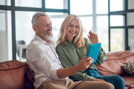 Online. Mature couple in sunglasses sitting on the sofa and having a video callの写真素材