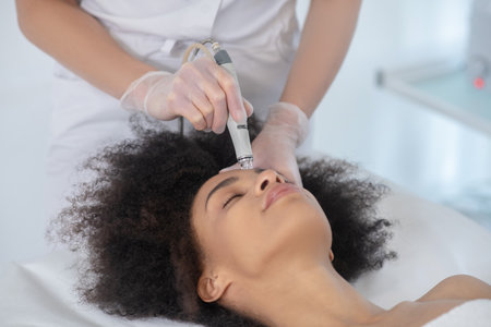 Cosmetological procedure. Face of girl lying on couch and hands of beautician doctor in gloves with...