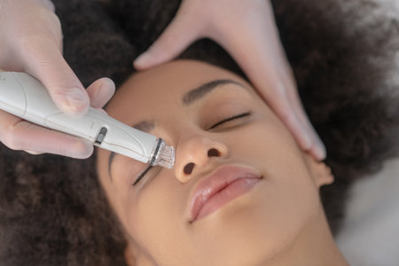 Skin care. Beautician hand holding special small apparatus near nose of young pretty girl with...