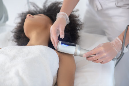 Cosmetology, new technology. Young girl with curly hair lying on couch during cosmetic procedure and...